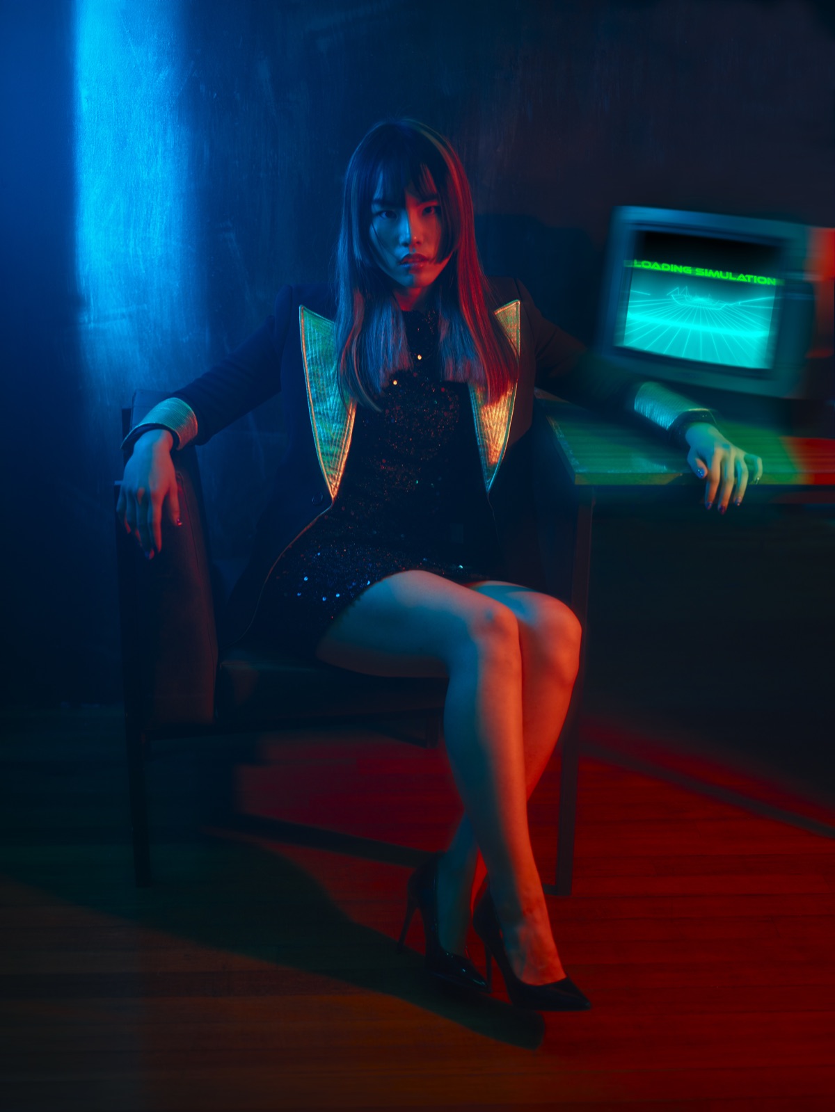 A seated model in a gold-lapelled jacket beside a retro monitor reading Loading Simulation.