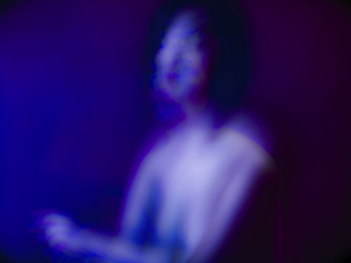 A soft-focus figure dissolving into fields of blue and magenta light.