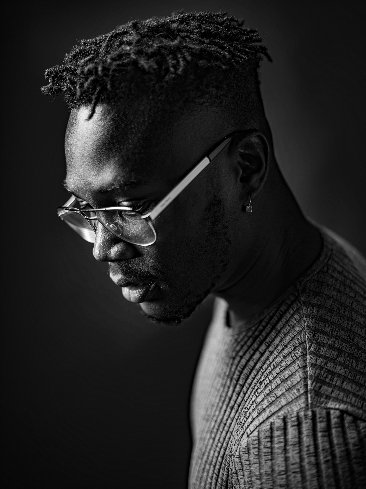 Black and white portrait of a man in glasses looking down, lit from the side.
