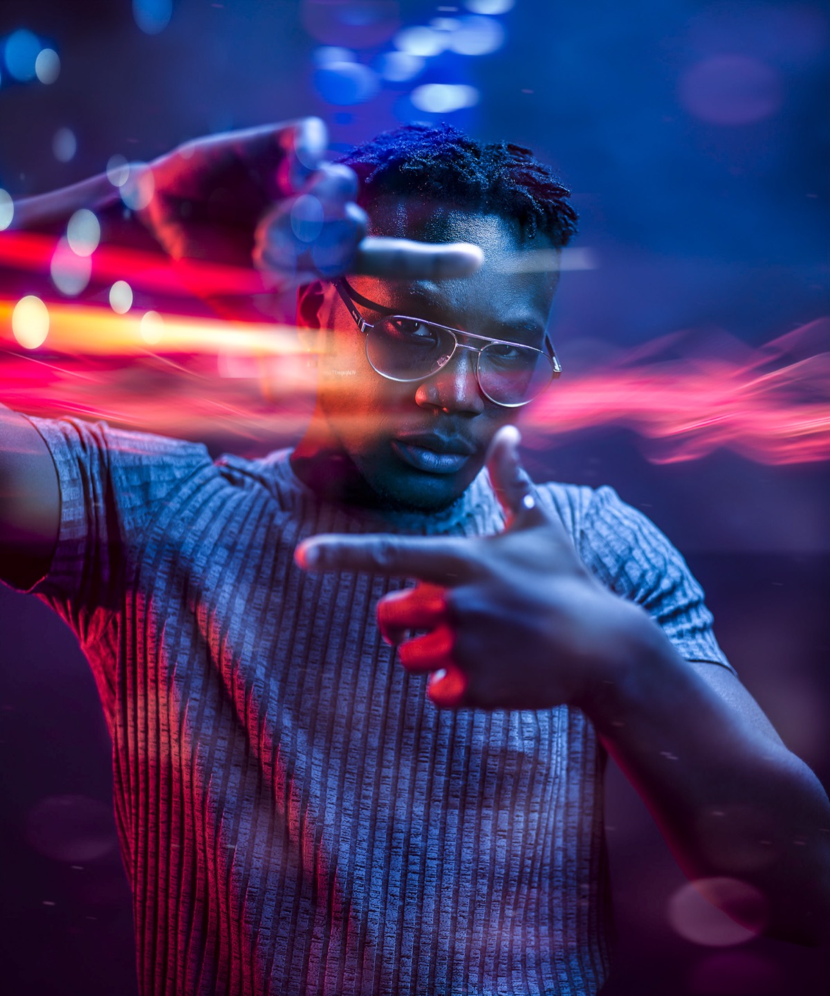 A man in glasses framing the shot with his hands, streaked with red and blue light trails.