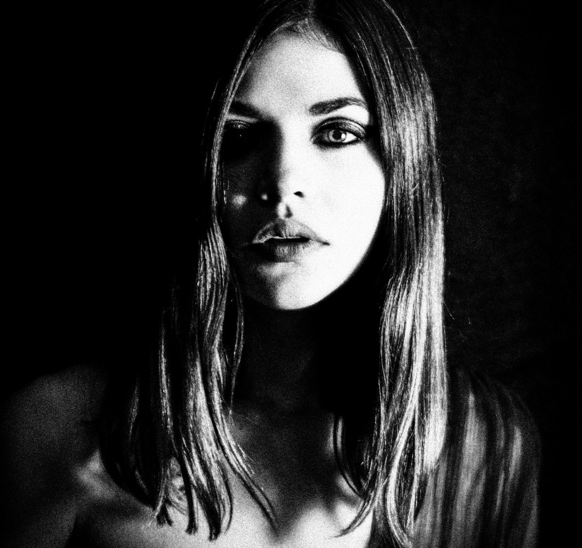 High-contrast black and white portrait of a woman emerging from deep shadow.